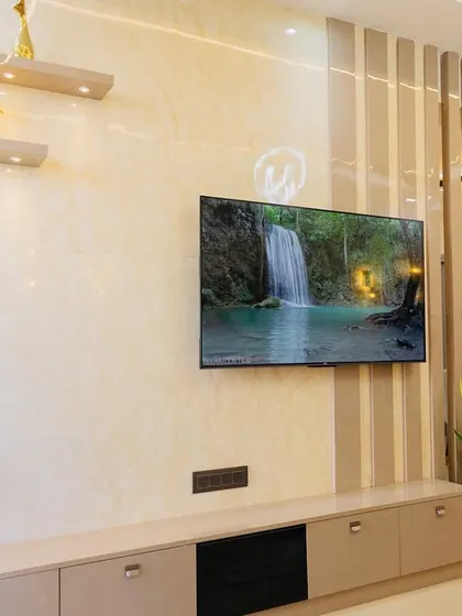 Standing next to a sleek TV unit in a recently completed project. The design combines a light-colored console with a textured wall panel and floating shelves, creating a modern and functional entertainment center.