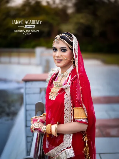 A full-length portrait of a Rajasthani bride. The vibrant red and pink attire, along with the traditional jewelry, showcases a complete look that our students learn to style.