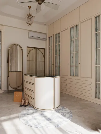 This classical dressing room features an elegant central island for accessories and ample wardrobe space with fabric-backed glass doors. The design is timeless, with a mix of curved and linear forms.