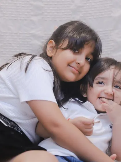The little brother smiles, snack in hand, while his sister holds him close. These are the real, everyday moments we love.