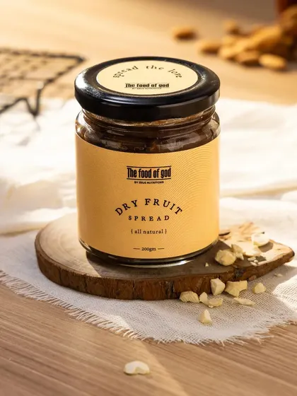 A warm, rustic shot of the Dry Fruit Spread. The use of a wooden coaster, natural fabric, and beautiful window-like lighting gives this image a cozy, homemade feel.