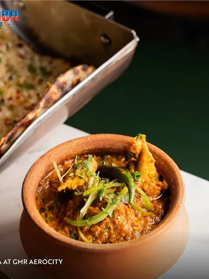 A close-up of a traditional chicken curry served in an earthen pot at Dhaba, alongside fresh naan. This image highlights the authentic presentation and rustic charm of my desi dining experiences.