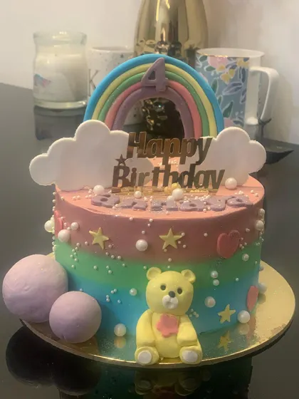 A colorful rainbow-themed cake with a cute yellow teddy bear. The pastel colors and fondant clouds make it a cheerful birthday choice.