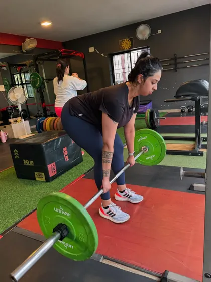 A client focuses on her deadlift form, with a tattoo symbolizing strength. We love seeing our clients embrace their power.