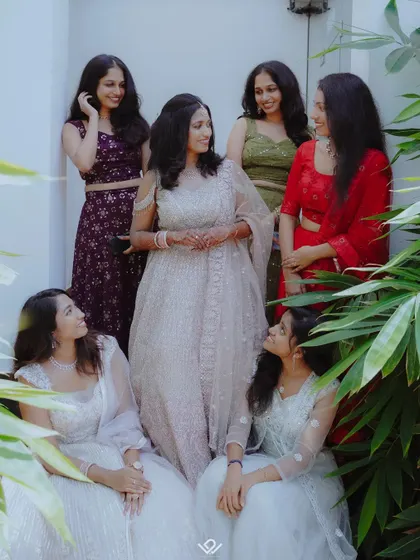 A bride and her friends share a happy moment, captured through a frame of green leaves.