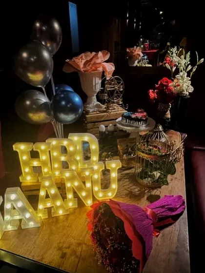I love setting up intimate table decorations for a birthday dinner. This arrangement includes "HBD JAANU" marquee letters, a bouquet of roses, balloons, and other decorative pieces to make the table feel special.