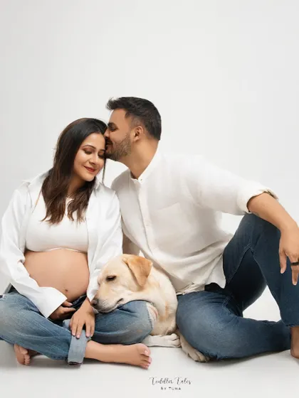 An expecting couple shares a quiet moment with their beloved dog resting its head on the mother's lap. This studio maternity portrait shows that family includes our furry members too, capturing the love that fills a home before a new arrival.