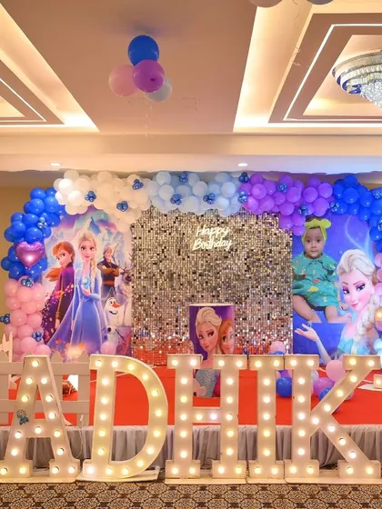 A magical Frozen-themed birthday party for Radhika. The stage includes a silver shimmer wall, character cutouts of Elsa and Anna, and large marquee letters spelling out the name.