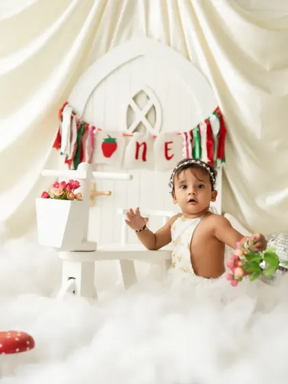A whimsical first birthday setup with a strawberry theme, featuring a white picket fence, clouds, and mushroom props. We can bring any creative vision to life.