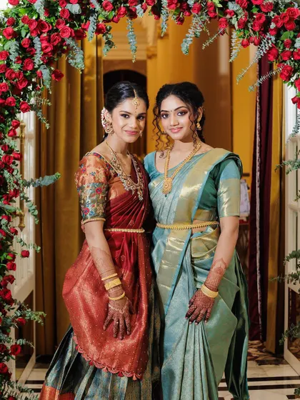Framed by a beautiful arch of red roses, the sisters look absolutely stunning. The makeup enhances their features while complementing the rich colors of their outfits.