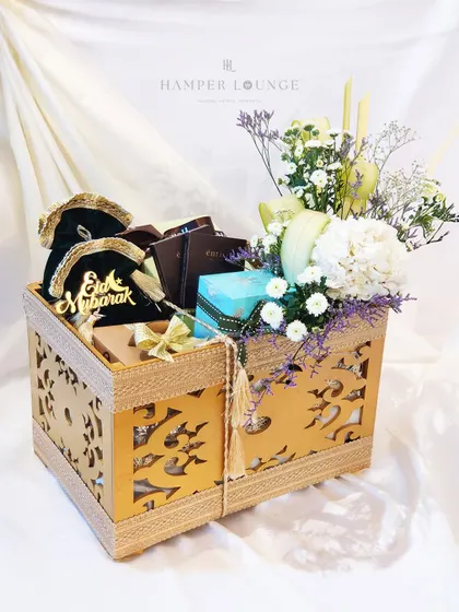 This ornate wooden box is perfect for a traditional Eid gift. It is filled with chocolates, treats in velvet pouches marked 'Eid Mubarak', and a small floral arrangement. The intricate design of the box itself becomes a cherished keepsake.
