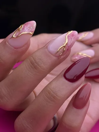 A sophisticated look for any celebration, featuring a deep maroon accent nail paired with pink marble and gold foil designs on almond-shaped extensions.