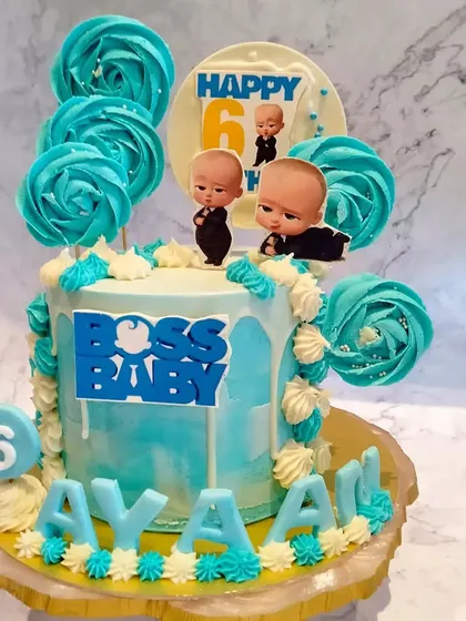 A Boss Baby themed cake for Ayaan's 6th birthday. The blue and white cake is decorated with lollipops and a "Boss Baby" logo.