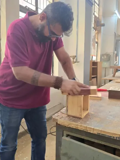 A student carefully sands the edges of a wooden box. The finishing process is just as important as the construction for achieving a professional result.