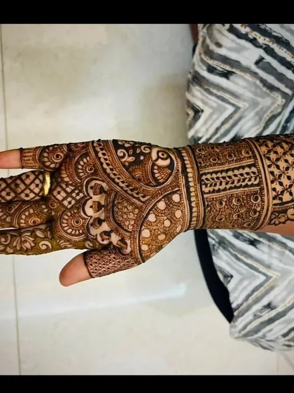 A detailed party mehendi design on the back of the hand, featuring a mix of geometric and floral patterns.