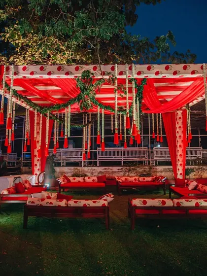 An intimate and traditional seating area for a pre-wedding ceremony. The design uses block-printed fabrics in red and white, with comfortable gaddas and hanging floral tassels.