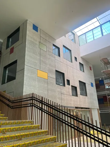 A new school building under construction, showing a feature wall with scattered, colorful window insets. This glimpse reveals how we integrate playful elements into the core architecture of the building.