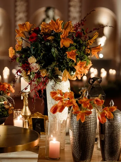 A centerpiece of orange lilies in a textured vase, surrounded by dozens of candles. The background of candle-lit arches creates a deeply romantic and mysterious atmosphere.