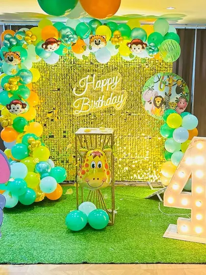 A compact jungle theme setup for a 4th birthday. It features a gold shimmer wall, a green turf floor, and marquee number '4', showing how we adapt our designs for different spaces.