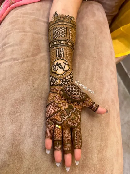 A stunning bridal mehndi design that extends up the arm. It features a personalized initial 'AV' and combines various patterns like checks, florals, and traditional motifs for a complete look.