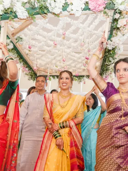 The bride's grand entrance at her Marathi wedding, walking under a floral canopy held by her family. Her radiant smile lights up the entire ceremony.
