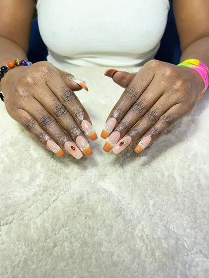 An orange glitter French tip with a single rhinestone accent. This is a warm and vibrant look, perfect for summer or festive occasions.