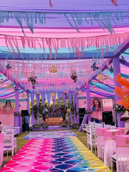 A full view of a lavender-themed Haldi event. The decor includes a colorful aisle runner, pastel drapes, and butterfly motifs hanging from the ceiling.