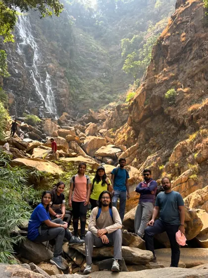 A group photo on the rocky terrain leading to a waterfall. The trek is as much a part of the adventure as the destination.