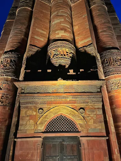 A close-up of the base of the Qutub Minar, showing the detailed calligraphic inscriptions and decorative bands.