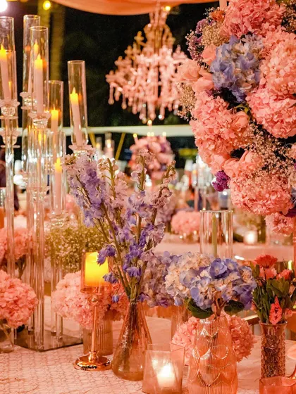 A close-up of the pastel-hued tablescape, showing the interplay of pink hydrangeas, lavender delphiniums, and glowing candles. The layering of colors and textures creates a rich and visually interesting design.