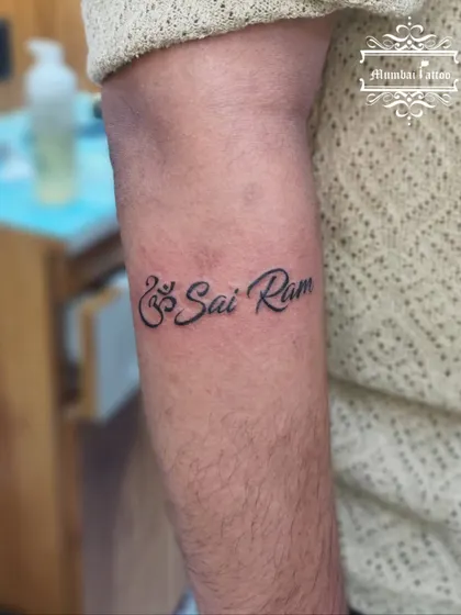 The devotional phrase "Om Sai Ram" tattooed on the forearm. We combine the sacred Om symbol with the name in a flowing script for a balanced and spiritual design.