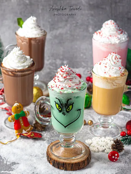 A fun collection of holiday-themed milkshakes and hot chocolates, including a playful Grinch-faced drink.