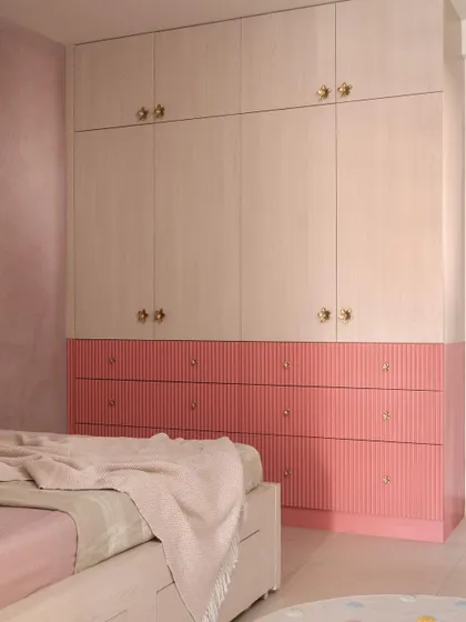 A closer look at a custom wardrobe I designed for a child's room, featuring a playful yet chic two-tone design. The fluted pink drawers add texture and color, while the light wood-finish upper cabinets with delicate gold knobs provide ample, stylish storage.