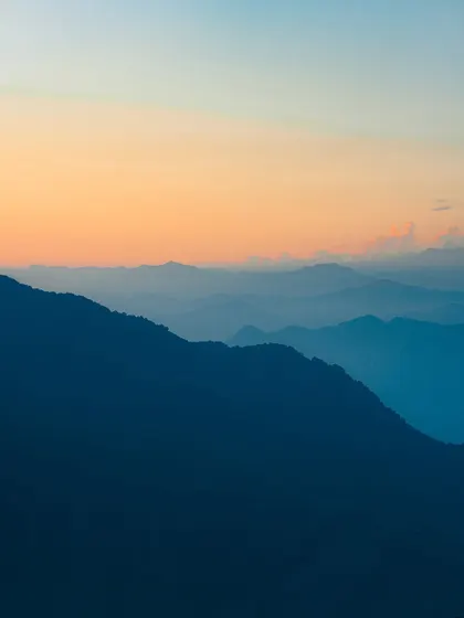 The beautiful layers of the mountains during a sunset in Mussoorie. The soft gradient of colors from orange to blue makes this a stunning example of landscape photography.
