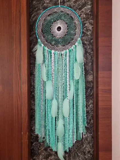 Infuse your space with serenity and charm. This simple yet elegant green dreamcatcher with soft feathers weaves its own special kind of magic.