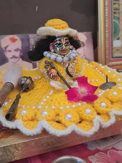 A simple yet elegant yellow woolen poshak, perfect for daily wear. This dress is adorned with white pearls along the scalloped edge and comes with a matching cap to keep your Laddu Gopal looking charming and feeling warm.