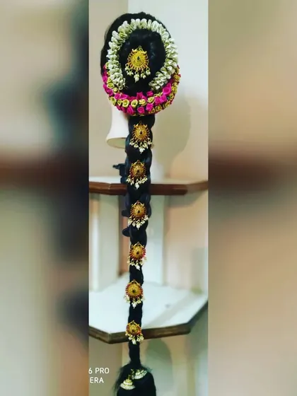 A detailed look at a traditional South Indian bridal braid, or 'poola jada'. This hairstyle is essential for a classic muhurtham look, featuring a long, thick braid decorated with fresh jasmine and rose petals, and accented with gold 'jadanagam' ornaments.