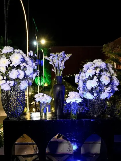 A close-up of white floral arrangements on a console table, with dramatic blue uplighting creating a moody and sophisticated atmosphere for an evening event.