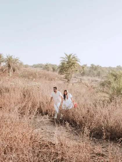 A wide shot of the couple walking through a field of tall, dry grass, adding a rustic and adventurous feel to their pre-wedding collection.