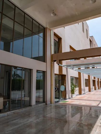 The covered walkway at Konark Academy features a polished marble floor that reflects the light from the glass facade. This corridor provides a sheltered transition space that is both functional and aesthetically pleasing.