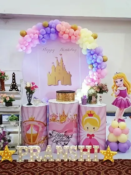 A classic princess theme for Pranshi's birthday. The setup includes a castle backdrop, cutouts of Princess Aurora, and pedestals decorated with royal motifs.