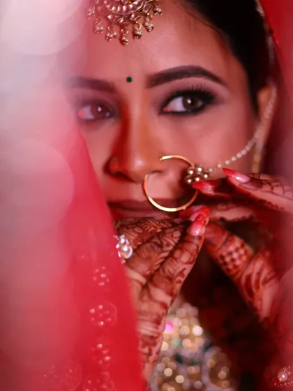 An artistic close-up of the bride's eyes and henna-adorned hands as she adjusts her nose ring.