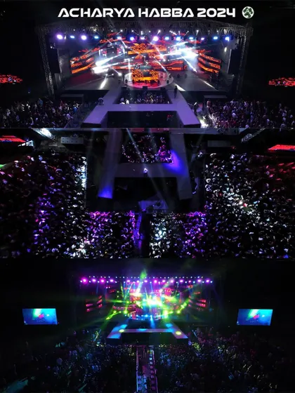 An aerial top-down shot capturing the immense crowd and spectacular stage lighting at Acharya Habba 2024. This perspective, only possible with professional drone videography, shows the sheer scale of the event and the energy of the audience.