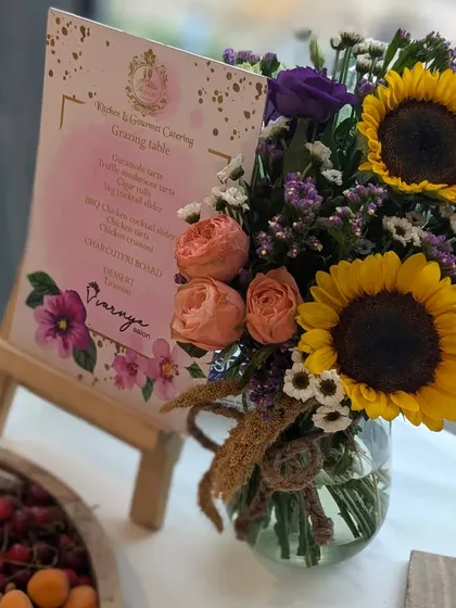 The menu is a key part of the experience. Here, a custom menu for a grazing table is displayed alongside a beautiful sunflower arrangement, setting the tone for the gourmet journey ahead.