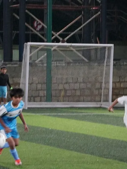 A young player skillfully controls the ball while being pursued by a defender.