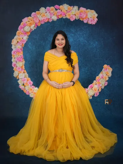 Let us bring your dreams to life with our creative prop setups. Here, our client shines in a vibrant yellow gown, seated on a floral crescent moon prop that adds a touch of magic and whimsy to her maternity portrait.