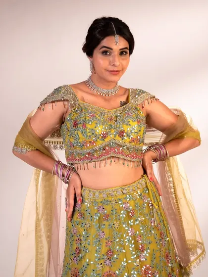 A close-up of the lime green lehenga's blouse. The delicate, multi-colored floral embroidery and tassel details on the shoulders are what make this piece so festive.