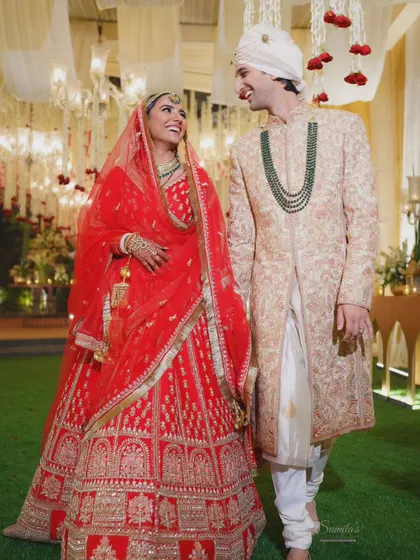 A candid moment of laughter between the bride and groom. Her vibrant red lehenga and his elegant sherwani are beautifully captured in this joyful wedding portrait.