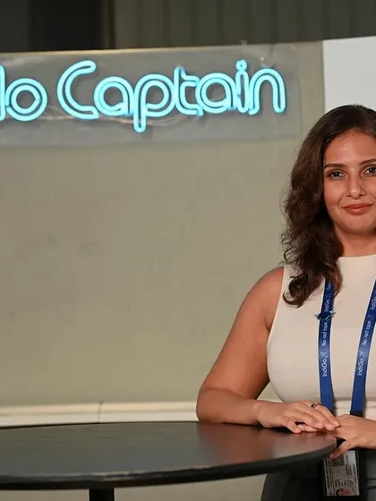 A confident portrait of an Indigo employee. The "Hello Captain" sign in the background adds a touch of brand personality to this professional shot.