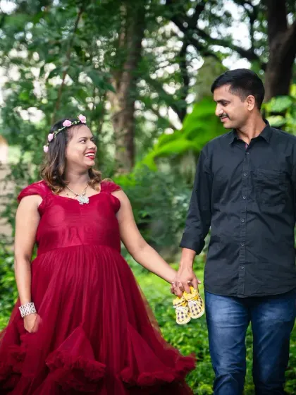 A lovely walk through a lush green path. The mom-to-be looks radiant in her red tulle gown, holding hands with her partner in this romantic outdoor maternity photo.